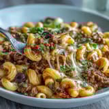 A close-up view of One-Pan High Protein Chili Mac topped with green onions, sour cream, and crushed tortilla chips.  