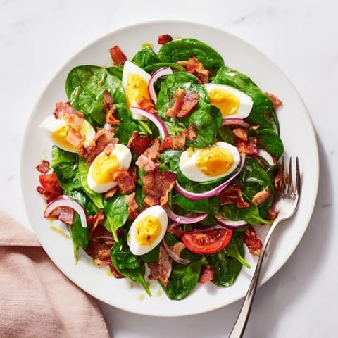 A serving bowl of Spinach Salad with Bacon, featuring baby spinach, halved cherry tomatoes, and red onion slices tossed in a homemade vinaigrette.