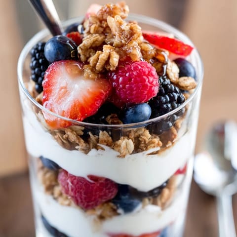 A close-up of Berry Parfait showing juicy strawberries and blueberries stacked with granola and honey drizzle.