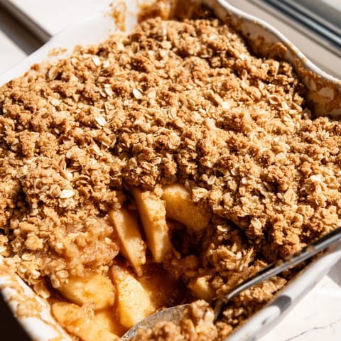 Warm Apple Crumble topped with crunchy oats and brown sugar, paired with a scoop of vanilla ice cream.