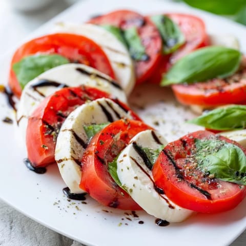 Fresh sliced tomatoes and creamy mozzarella arranged in a Caprese Salad on a platter, drizzled with balsamic glaze and olive oil.