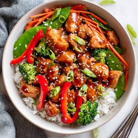 Steamed rice and colorful vegetables topped glazed Teriyaki Chicken Bowl garnished with sesame seeds and scallions.