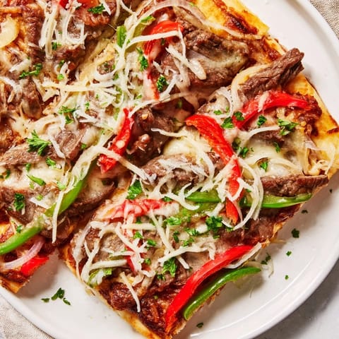 Tender ribeye steak and onions mingle under melted provolone on this crispy Philly Cheesesteak Pizza slice.