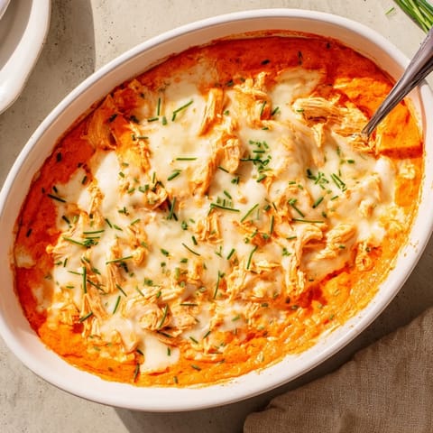 Golden, cheesy Buffalo Chicken Dip baked in a dish, topped with chopped chives.