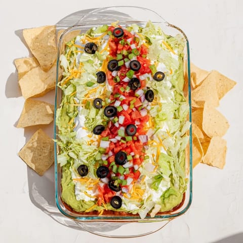 A chilled Tex-Mex Seven-Layer Dip with cheddar, Monterey Jack, and fresh toppings for a party appetizer.