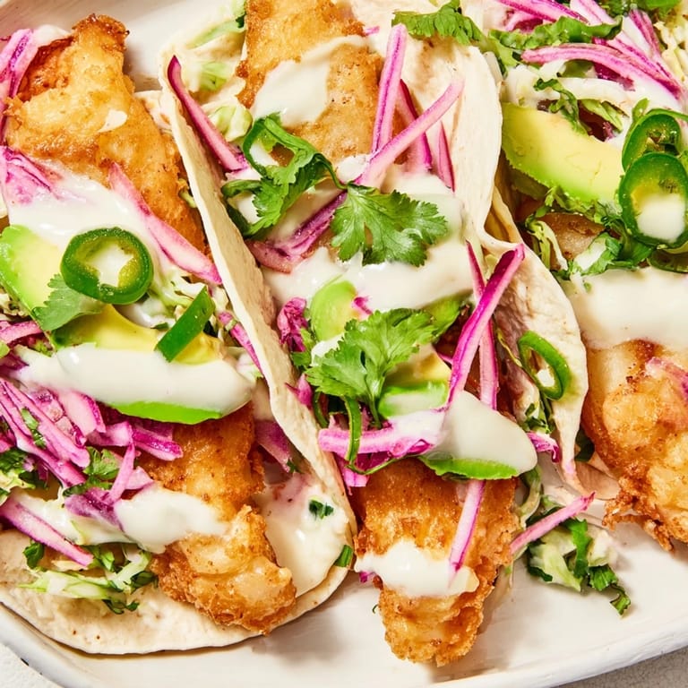 Fresh Baja Fish Tacos on corn tortillas with avocado, cilantro, and lime wedges.
