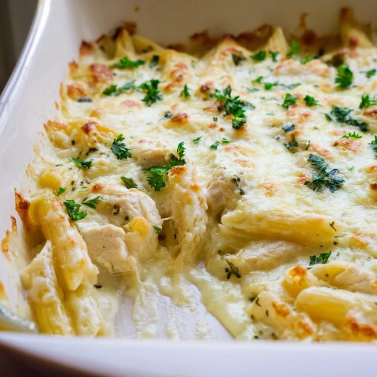 Steam rises from a spoonful of creamy Chicken Alfredo Bake, revealing tender penne pasta and juicy diced chicken.