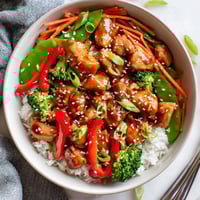 Steamed rice and colorful vegetables topped glazed Teriyaki Chicken Bowl garnished with sesame seeds and scallions.