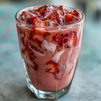 A refreshing Pink Starburst Refresher with vibrant berry and citrus flavors, served over ice with fresh strawberry slices.